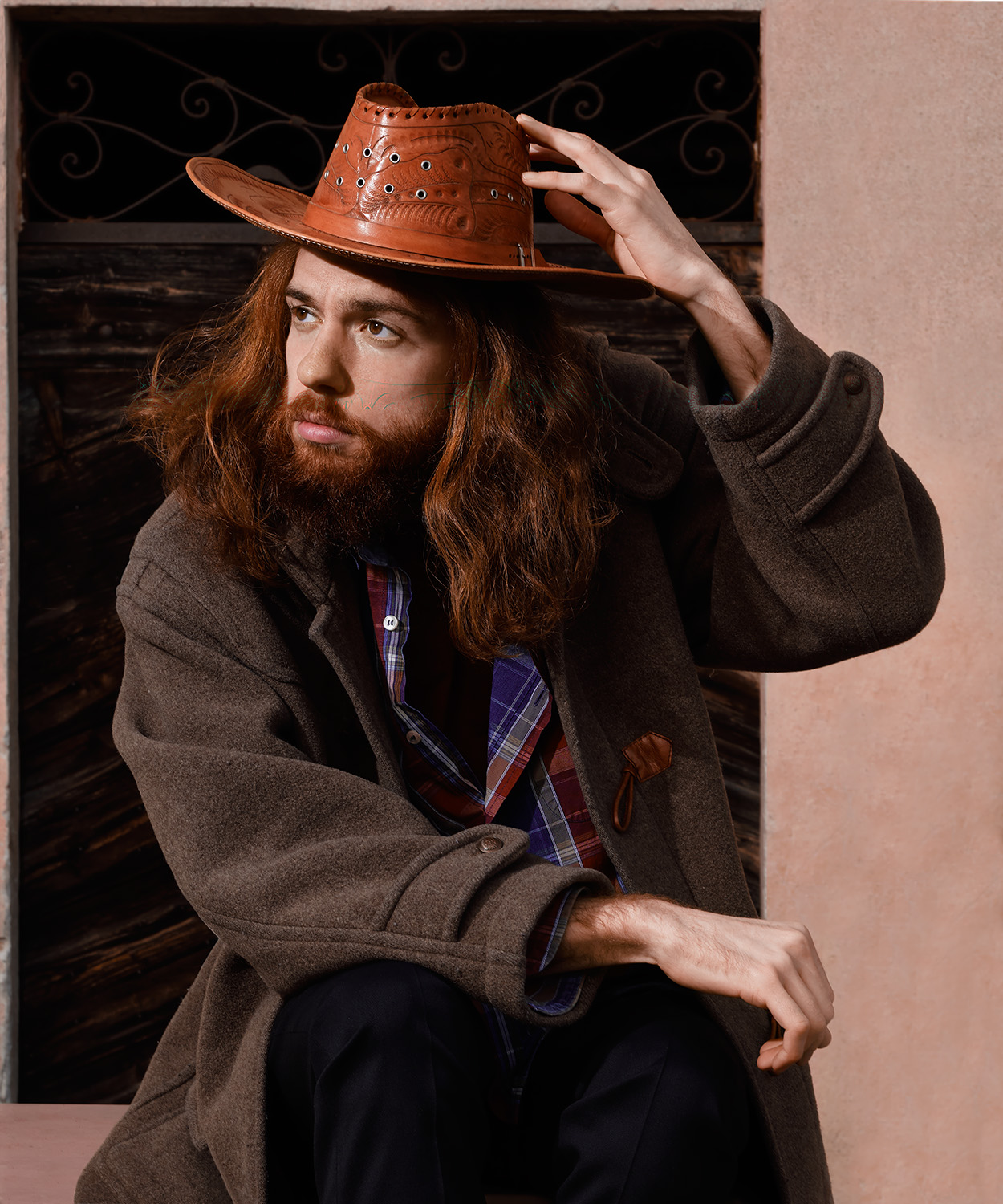 Ritratto di un uomo con capelli lunghi, barba e cappello di cuoio, davanti a una porta di legno
